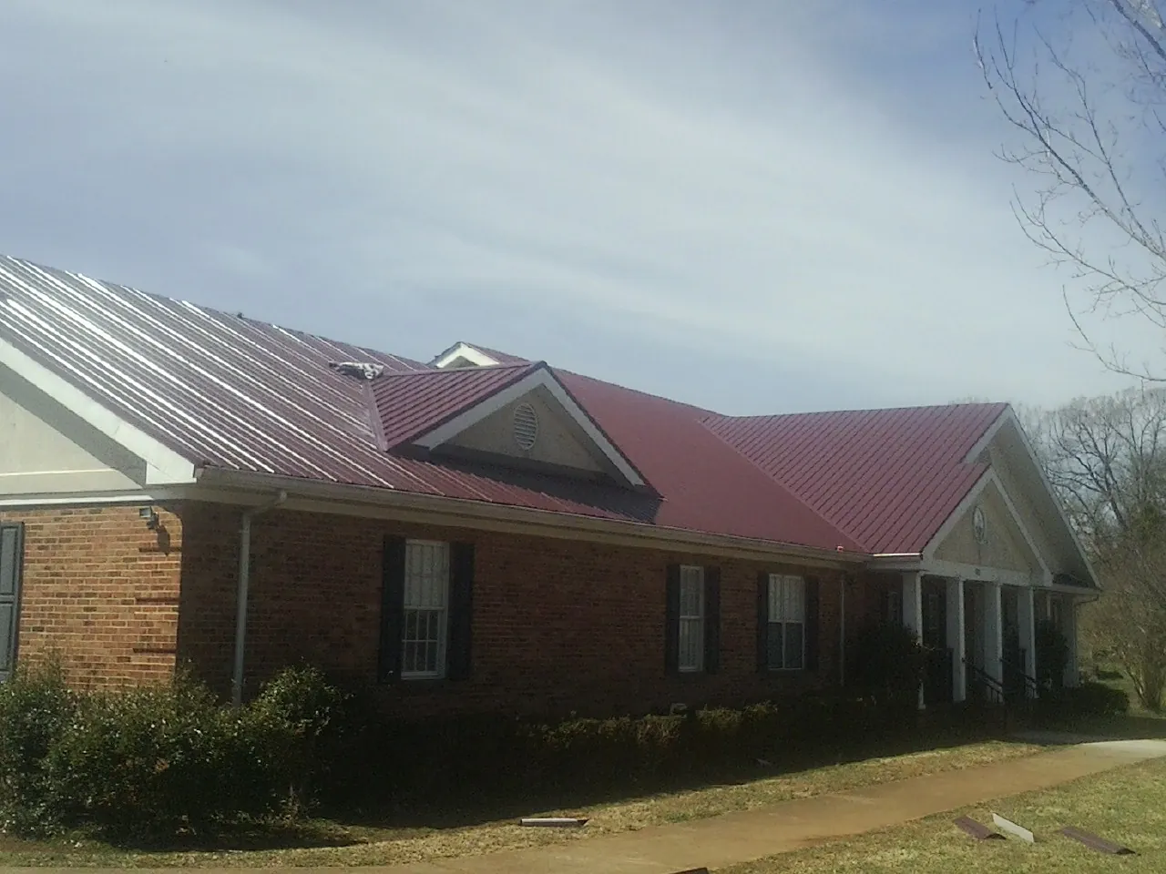 Red metal roof with gabled entries on a long brick building, from a Hail Damage Roof Repair job in Aiea