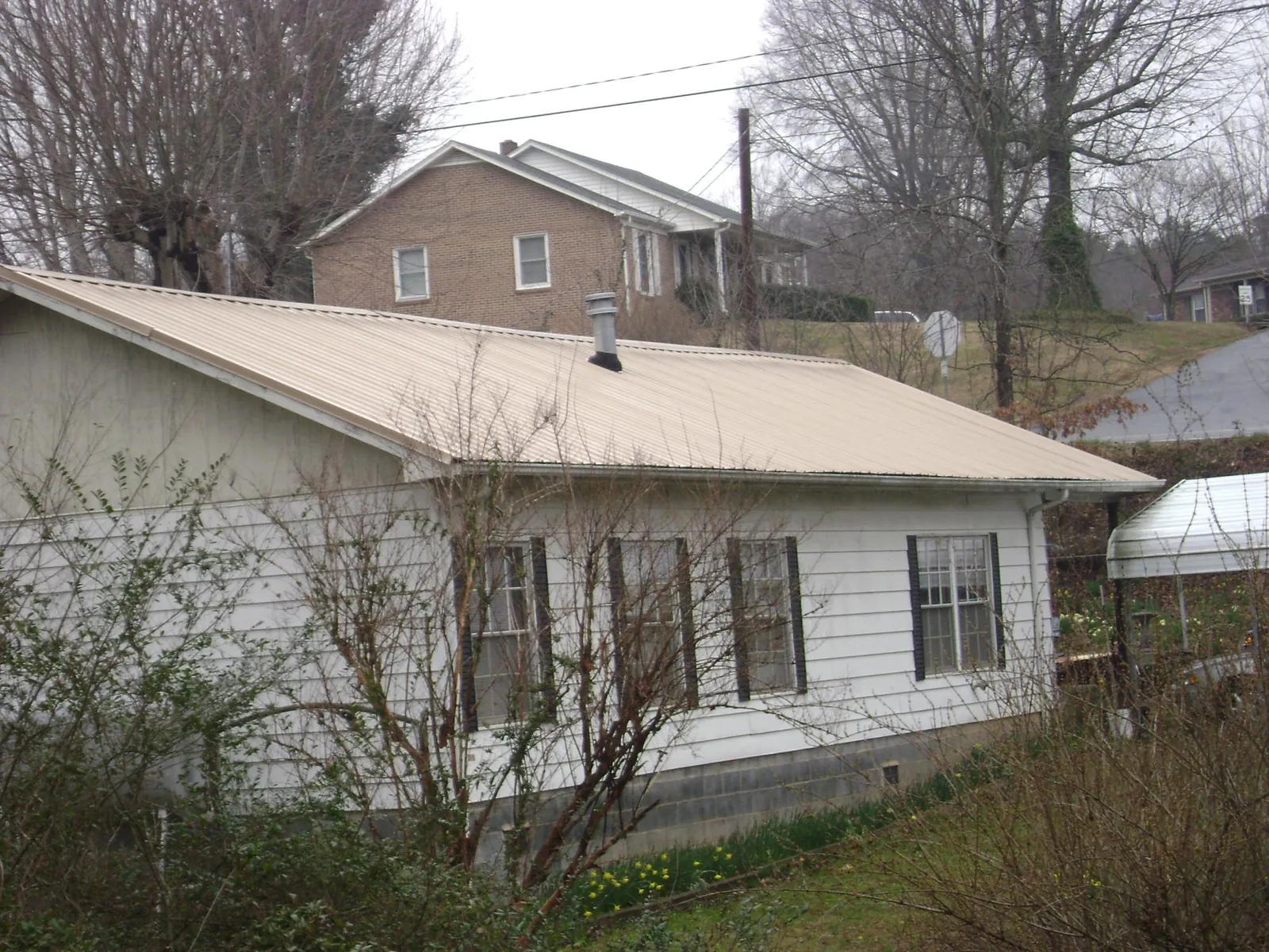 Tan metal roof on a white sided house set into a hillside — Commercial Roofing by Roofing Brothers in Aiea